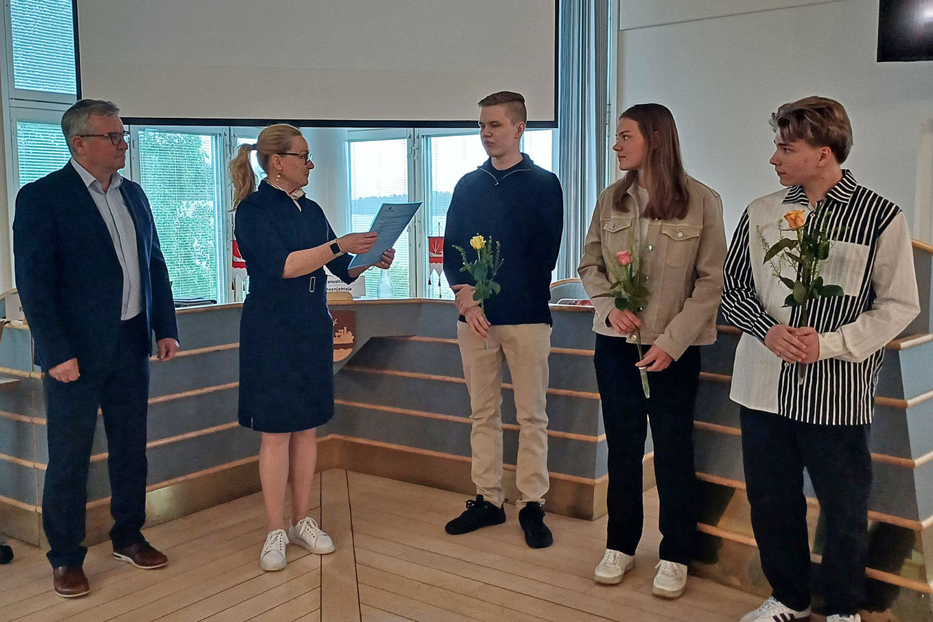 Viisi henkilöä, joista kolmella on kädessään ruusut.