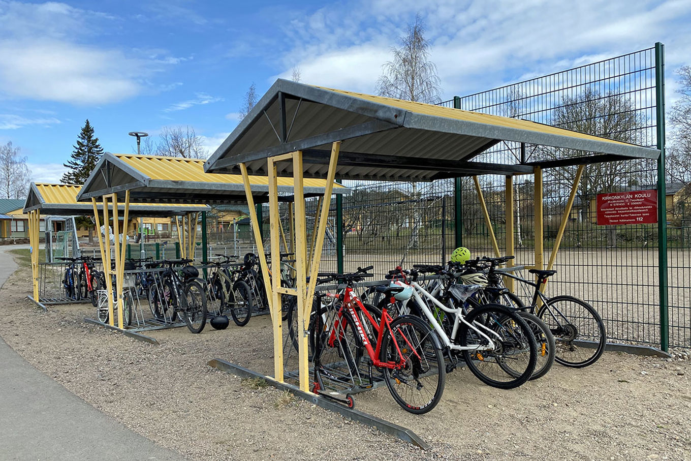 Kolme keltaista pyöräkatosta, joiden alla on erivärisiä pyöriä. Taustalla näkyy hiekkakenttää.