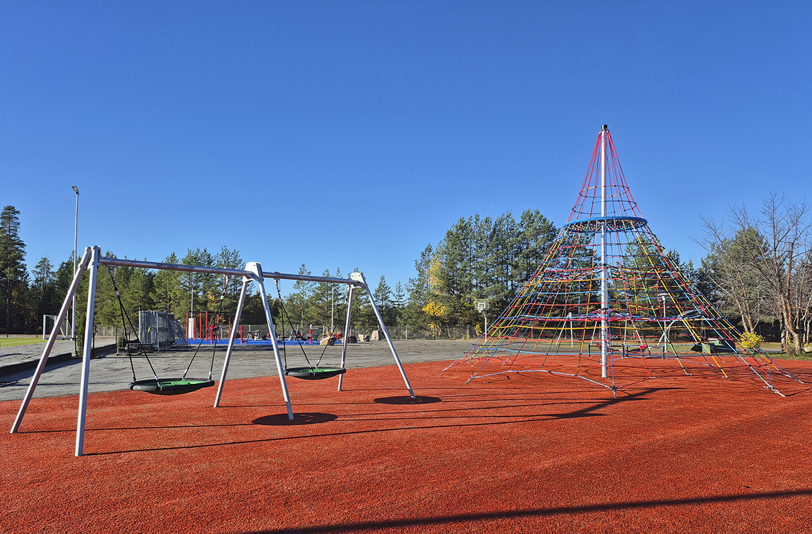 Kaksi keinua ja kiipeilyteline. Taustalla näkyy metsää.