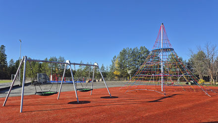 Kaksi keinua ja kiipeilyteline. Taustalla näkyy metsää.