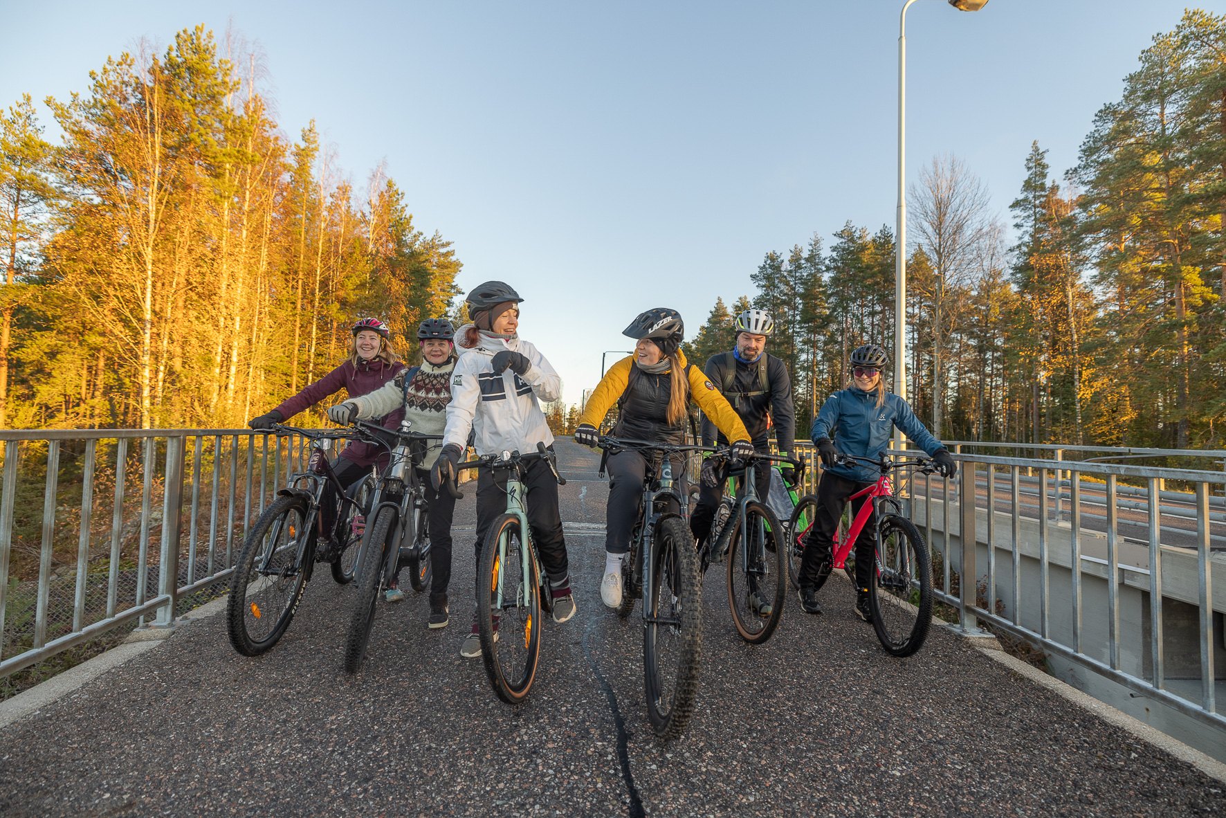 Iloisesti hymyileviä pyöräilijöitä sillalla.